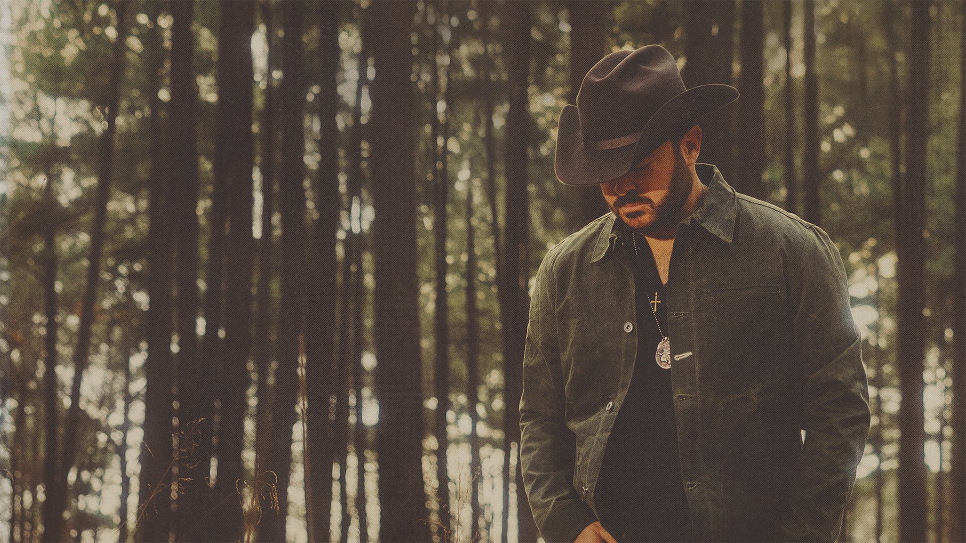 Wade Bowen wearing a cowboy hat and dark jacket standing in a forest