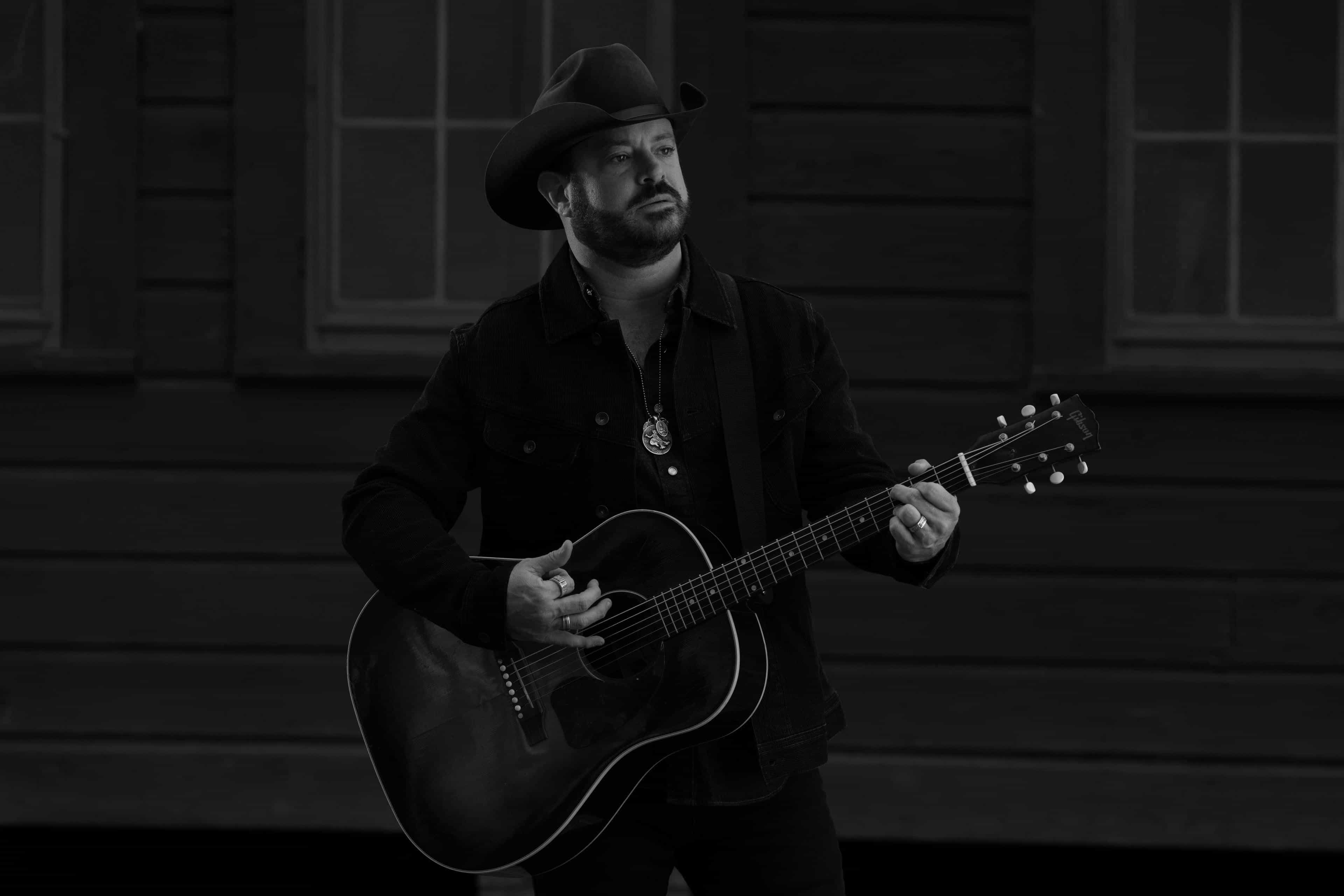 Black and white photo of Wade in front of a historic building holding a guitar